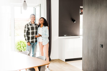 Obraz premium full length view of african american husband and wife hugging and looking at room