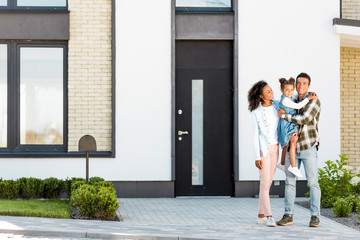 full length view of african american family standing near new house while father holding kid and...