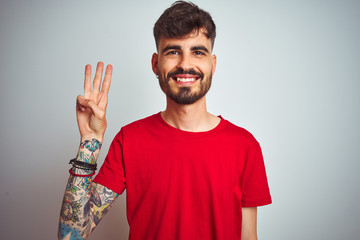 Young man with tattoo wearing red t-shirt standing over isolated white background showing and pointing up with fingers number three while smiling confident and happy.