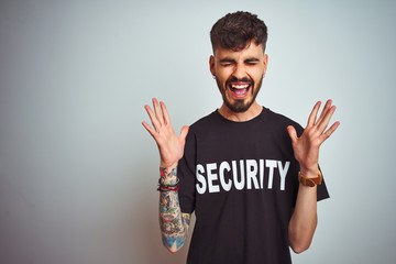 Young safeguard man with tattoo wering security uniform over isolated white background celebrating...