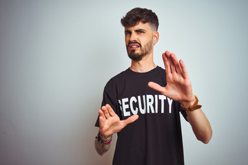 Young safeguard man with tattoo wering security uniform over isolated white background afraid and...