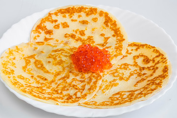 Stack of homemade thin pancakes with red caviar on a wooden cutting board over dark rustic slate,stone or metal background.Top view .