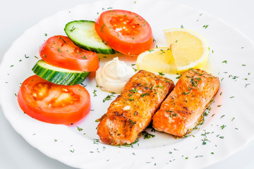 two large pieces of grilled salmon grilled with lemon, white plate with tomatoes and cucumbers, top view