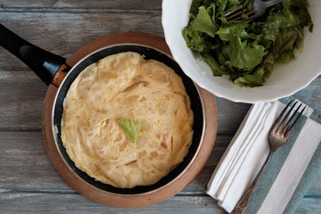 Spanish omelet in the pan and lettuce salad and onion