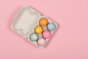 Easter background with a carton egg box with pastel colored easter eggs in it on a pink background