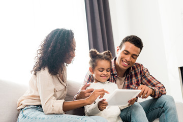 kid holding digital tablet while african american mother showing something with finger and dad looking at tablet