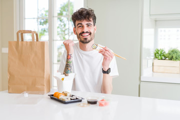 Young man eating asian sushi from home delivery screaming proud and celebrating victory and success very excited, cheering emotion