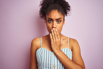 Fototapeta na wymiar African american woman wearing casual striped dress standing over isolated pink background cover mouth with hand shocked with shame for mistake, expression of fear, scared in silence, secret concept