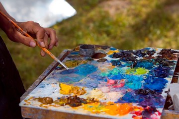 painter's skilful hand mixes oil paints with a brush on wooden palette, stained with a fresh...