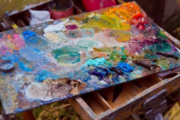painter's wooden palette stained with a mess of fresh mixed colorful oil paints, rests on easel after artistic painting plainair, creative disorder