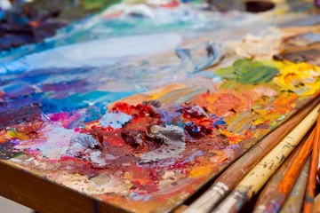 painter's wooden palette in disorder with mixed fresh bright oil paints at summer plainair painting...