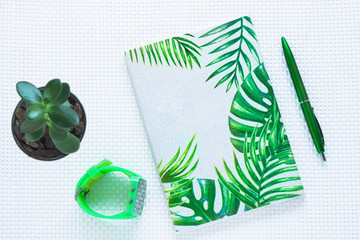 Green fashion notebook and pen on white textured background. Top view, flat lay