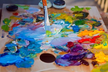 painter's wooden palette covered with a mix of fresh bright oil paints, brush with a green paint,...