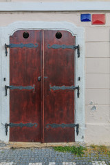 Historic closed wooden door on a building wall. Brown door with black metal fittings. bright wall with street sign and house number. walkway with paving stone