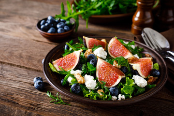 Fig salad with goat cheese, blueberry, walnuts and arugula on wooden background. Healthy food. Lunch