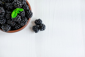 Background for a banner with blackberry berries on a light wooden background. Close-up photo of blackberries with copy space and mint leaves. Flat lay, top view.