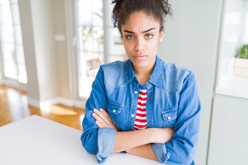 Beautiful young african american woman with afro hair wearing casual denim jacket skeptic and...