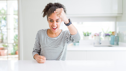 Beautiful african american woman with afro hair wearing casual striped sweater angry and mad raising fist frustrated and furious while shouting with anger. Rage and aggressive concept.