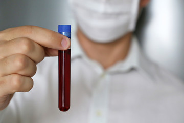 Test tube in male hand close up, man in medical mask holding a vial with red liquid. Concept of blood sample, medical and chemical research, vaccination, doctor or scientist