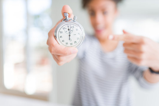 Young african american woman holding stopwatch very happy pointing with hand and finger