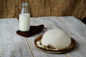  Cow's milk in a glass bottle and homemade cottage cheese in a ceramic plate, lie on a wooden tabletop in the background, sackcloth.