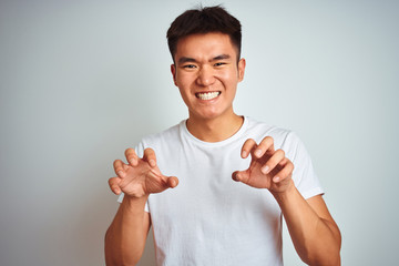 Young asian chinese man wearing t-shirt standing over isolated white background smiling funny doing claw gesture as cat, aggressive and sexy expression