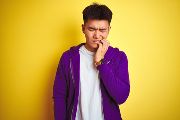 Obraz premium Young asian chinese man wearing purple sweatshirt standing over isolated yellow background touching mouth with hand with painful expression because of toothache or dental illness on teeth. 