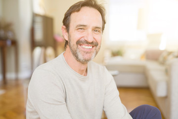 Handsome middle age man sitting on the floor smiling at the camera at home