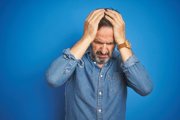 Handsome middle age senior man with grey hair over isolated blue background suffering from headache desperate and stressed because pain and migraine. Hands on head.