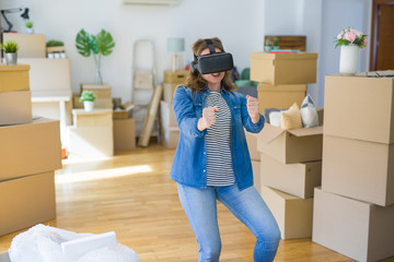Young blonde woman wearing virtual reality glasses playing a simulation game around cardboard boxes moving to a new house