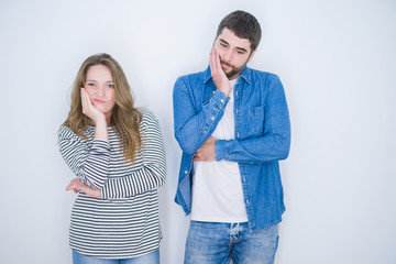 Young beautiful couple standing together over white isolated background thinking looking tired and bored with depression problems with crossed arms.