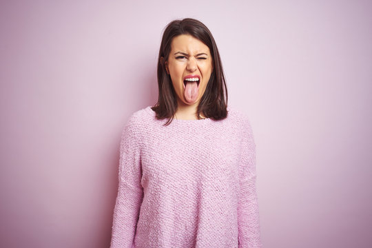 Young beautiful brunette woman wearing a sweater over pink isolated background sticking tongue out happy with funny expression. Emotion concept.