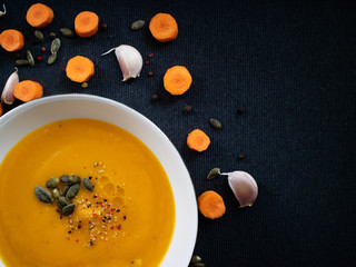 Top view of a white plate with vegetable soup made of carrot and pumpkin