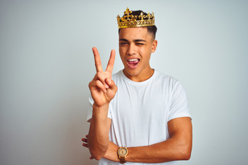 Young brazilian man wearing king crown standing over isolated white background smiling with happy...