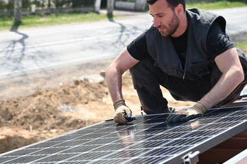 Technicians installing alternative energy photovoltaic solar panels on roof 
