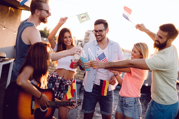 Obraz premium Young friends having fun at a rooftop party, playing the guitar, singing, dancing and drinking