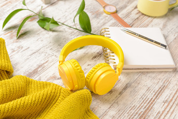 Modern headphones, warm sweater and notebook on light wooden background