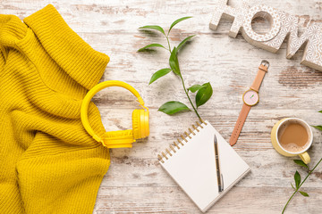 Composition with modern headphones, warm sweater, notebook and cup of coffee on light wooden background