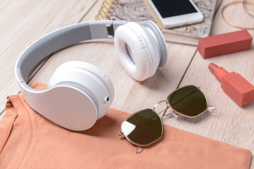 Modern headphones, sunglasses, t-shirt and cosmetics on wooden background