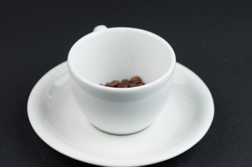 White cup of coffee and coffee beans isolated on black background