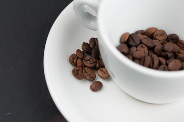 White cup of coffee and coffee beans isolated on black background