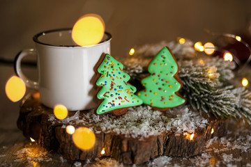 Fototapeta na wymiar Holiday traditional food bakery. Two gingerbread green christmas trees in cozy decoration with garland lights and cup of hot coffee