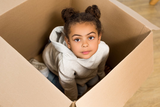 High Angle View Of Cute Child Sitting In Box And Looking At Camera