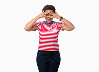 Fototapeta premium Beautiful young african american woman wearing glasses over isolated background peeking in shock covering face and eyes with hand, looking through fingers with embarrassed expression.