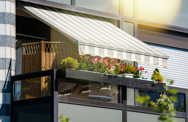 French balcony with beautiful awning and flowers covered with rays of sun - protection during hot weather and radiation - obrazy, fototapety, plakaty