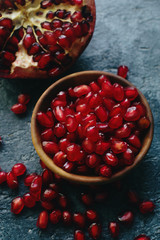 Fresh organic juicy pomegranate seeds in wooden bowl on dark stone background