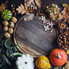 Autumn background with decorative pumpkin, acorns, nuts, greens, autumn leaves and wooden board with space for text on dark stone table