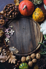 Autumn background with decorative pumpkin, acorns, nuts, greens, autumn leaves and wooden board with space for text on dark stone table
