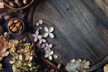 Autumn background with decorative pumpkin, acorns, nuts, greens, autumn leaves and wooden board with space for text on dark stone table