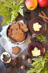 Autumn mood: cinnamon cookies in form of maple leaves, two cups of tea, red apples and yellow leaves